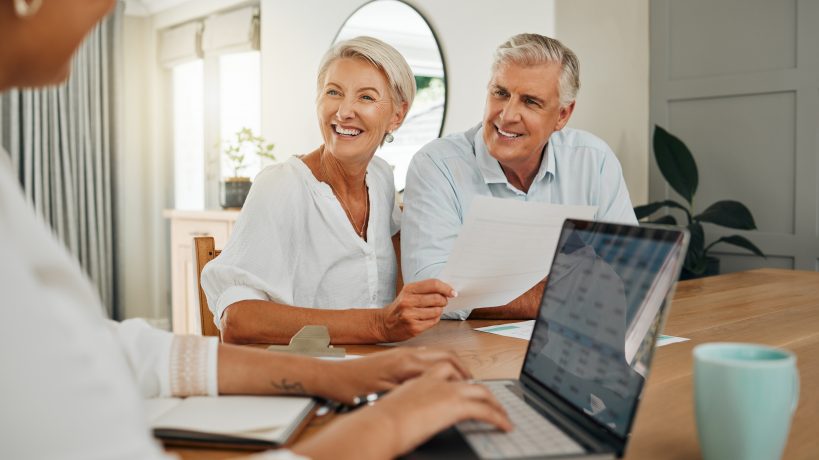 Retirement, savings and couple planning finance, insurance and investments in living room. Man and woman and seniors communication, talking and discuss wealth with internet banking and laptop at home.